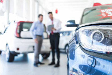 Car saleman making deal with buyer in background with new car in foreground